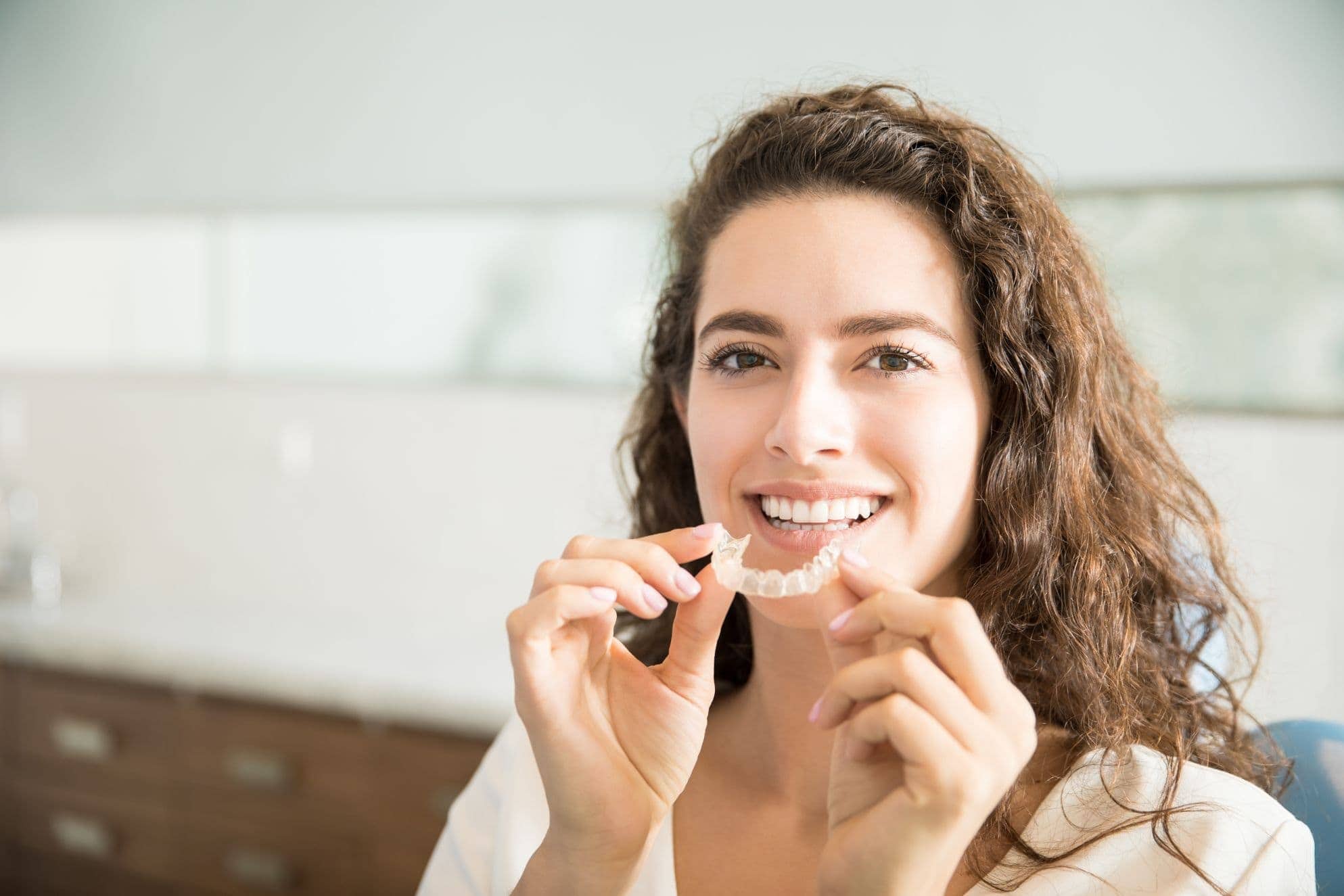 A woman shows the clear aligners she uses as part of her orthodontic treatment.